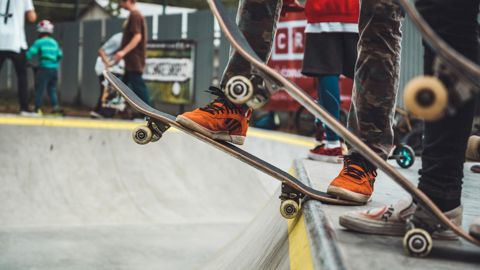 A close-up photo of the ;egs and skateboards of three young people preparing to 'drop in' from a skate ramp.