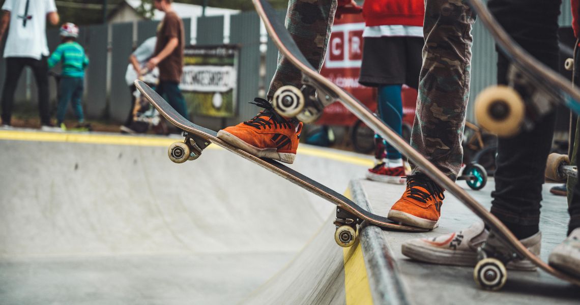 A close-up photo of the ;egs and skateboards of three young people preparing to 'drop in' from a skate ramp.